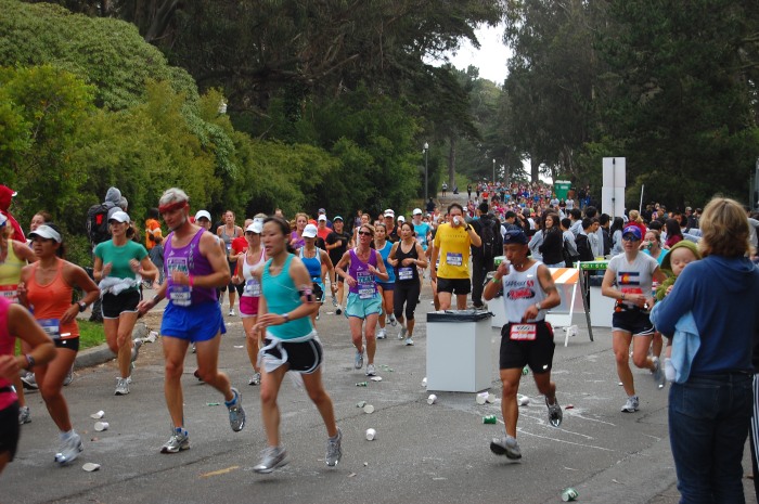 Full and half marathoners meet at an aid station in the park.